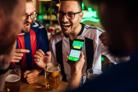 Soccer fans drinking beer at the pub and using mobile app for betting.